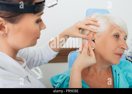doctor helping elderly woman inserting hearing aid Stock Photo