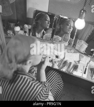 Cosmetics in the 1940s. A young woman at home is sitting at a make up desk and looking at herself in mirrors from diffente angles while putting on makeup. There are many different kinds of cosmectics lying on the table in front of her. Sweden 1944.  Photo Kristoffersson AB3-8 Stock Photo