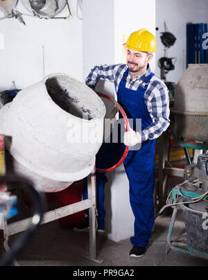Young smiling guy using concrete mixer for construction work at workshop Stock Photo