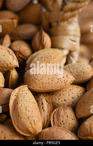 macro of organic almonds in their shells full frame image with an old wicker baskets vertical with selective focus in background and foreground to ad  Stock Photo
