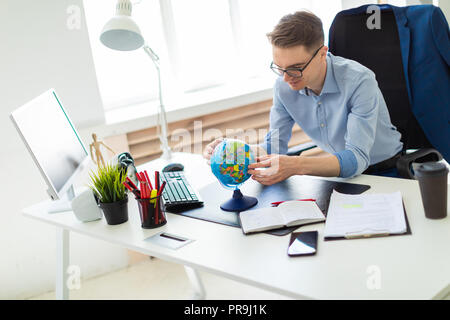A handsome young man with glasses, blue trousers and a light shirt is working in the office. On the back of the chair hangs his jacket. photo with dep Stock Photo