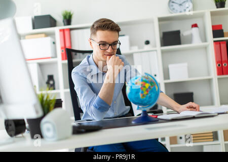 A handsome young man with glasses, blue trousers and a light shirt is working in the office. On the back of the chair hangs his jacket. photo with dep Stock Photo