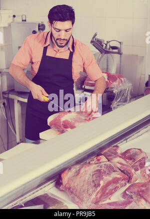 happy germany man butcher is cutting meat on his workplace in the market. Stock Photo