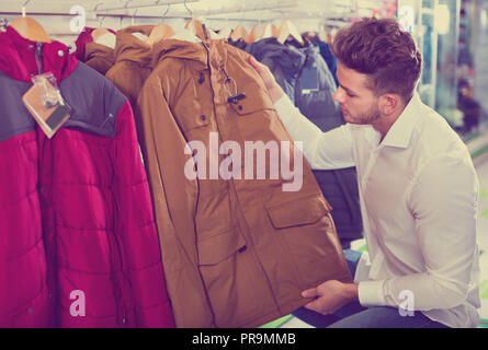 Young positive man choosing new coat in sports store Stock Photo