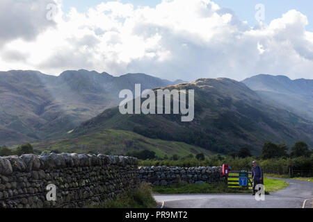 A hillwalker returning from the mountains after descending The Band with Crinkle Crags on left and Bowfell on right. Great Langdale, Lake District, Cu Stock Photo