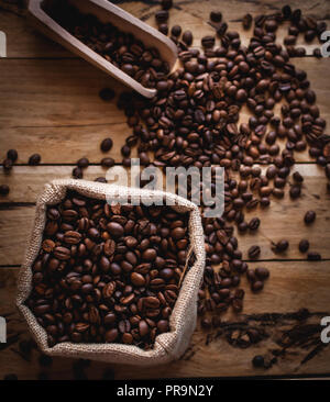 Coffee beans in jute sack and scoop on wooden background, top view Stock Photo
