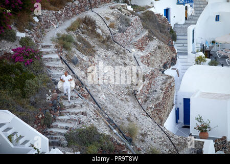 man walking down the cliff via steps  Oia landmark blue dome churches Santorini, a Cyclades group of islands in Greece, tourists walking up the steep  Stock Photo