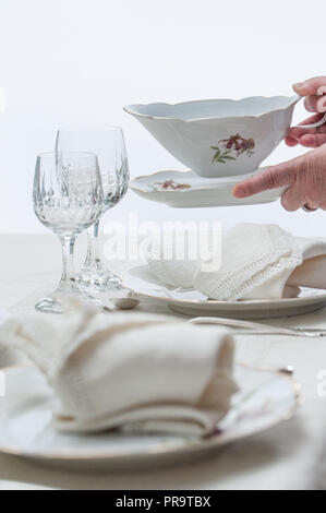 Women hands placing a saucer on a table served with porcelain dinnerware. Selective focus. Stock Photo