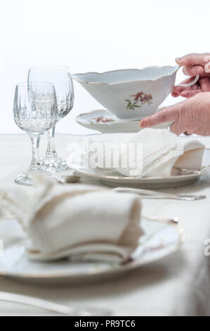 Women hands placing a saucer on a table served with porcelain dinnerware. Selective focus. Stock Photo