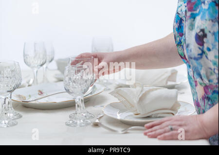 Women hands serving a crystal glassware of a table served with porcelain dinnerware. and vintage tablecloth. Selective focus. Stock Photo
