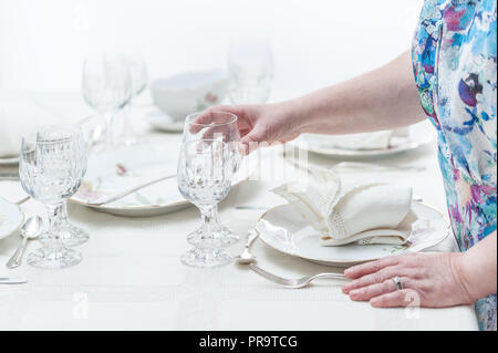 Women hands serving a crystal glassware of a table served with porcelain dinnerware. and vintage tablecloth. Selective focus. Stock Photo