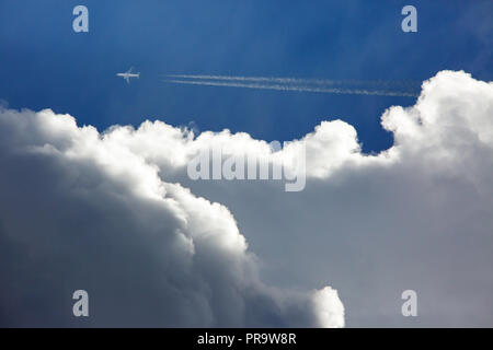 A commercial airliner flying at high altitude in a deep blue sky above threatening storm clouds. Stock Photo