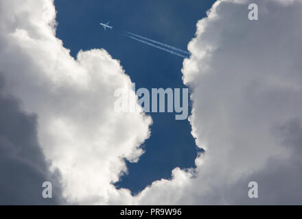 A commercial airliner flying at high altitude in a deep blue sky above threatening storm clouds. Stock Photo