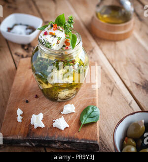 Marinated feta cheese in olive oil, herbs and red pepper flakes on wooden background Stock Photo