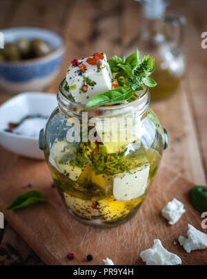 Close-up of marinated feta cheese in olive oil, herbs and red pepper flakes on wooden background Stock Photo