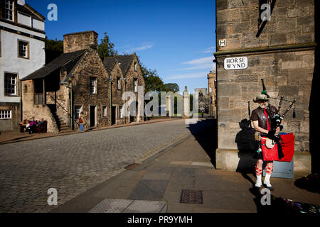 Historic Edinburgh, Scotland ,  Royal Mile  a pipper plays bagpipes to tourists for money with Sanctuary buildings on Abbey Strand behind Stock Photo
