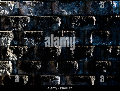 Aged worn grungy cement block wall with dirt and moss showing angled light Stock Photo