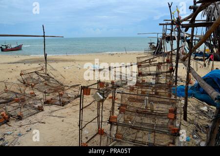 Wire mesh square box fishing nets and boats at seaside beach village Pattani Thailand Stock Photo