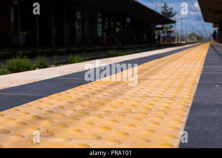 Low angle view of a safety yellow line on a train station with blue sky in the background. No people. Stock Photo