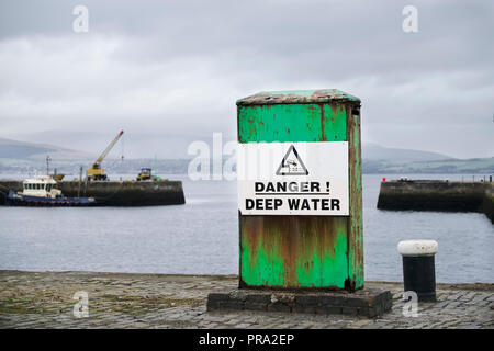 Danger deep water sign at sea harbour dock on green structure and boats in background Stock Photo