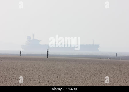 A tanker on the Mersey estuary passes Antony Gormley’s Another Place at Crosby in a light mist Stock Photo