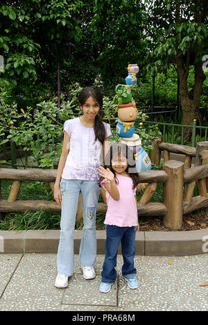 TWO SISTERS POSING FOR A  PORTRAIT IN FRONT OF THE HONEY POTS OF WINNIE THE POOH AT HONG KONG DISNEYLAND Stock Photo