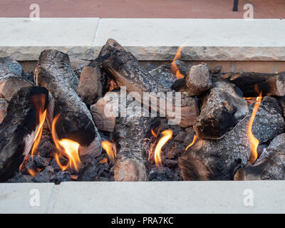 Logs sitting in open fire in a white stone firepit Stock Photo