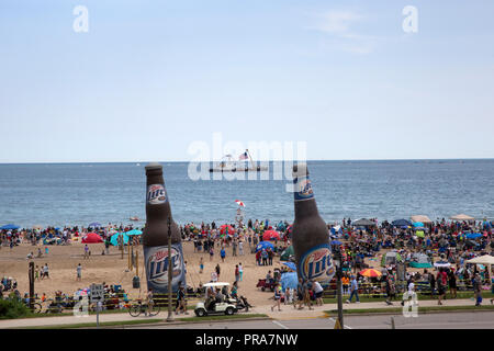 Crowd at the beach along the shores of Lake Michigan awaiting the start of the Milwaukee Air and Water Show.  A US Coast Guard ship is anchored in har Stock Photo