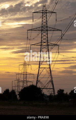 Electricity pylons or transmission towers carrying high voltage power lines and overhead cables above land as part of the national grid network supply Stock Photo