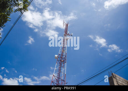 Red and white tell telephone signal cell tower rises up against a summer's blue sky Stock Photo