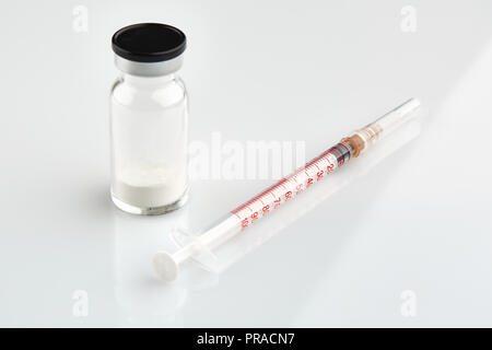 Small sealed bottle with medicine and syringe on white background. Stock Photo