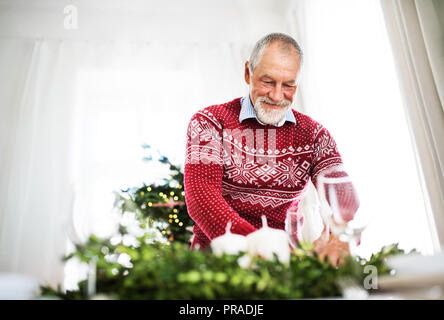 A senior man setting a table for a dinner at home at Christmas time. Stock Photo