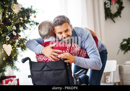 A hipster man hugging his senior father in wheelchair at Christmas time. Stock Photo