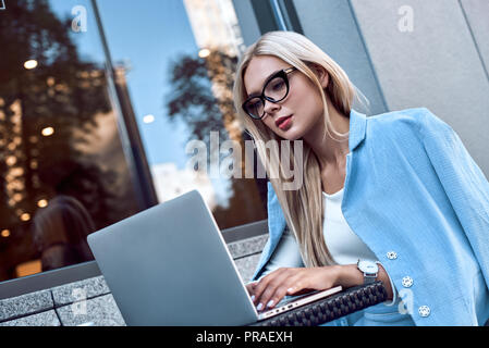 Fashionable businesswoman in glasses sitting in a cafe working with a laptop, her face is focused Stock Photo