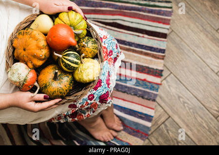 Young woman in white dress holding a basket with decorative pumpkins on her lap. Stock Photo