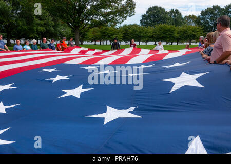 USA Maryland MD Baltimore Fort McHenry visitors hold up a large replica of the flag that was flying when Francis Scott Key wrote the Anthem poem Stock Photo