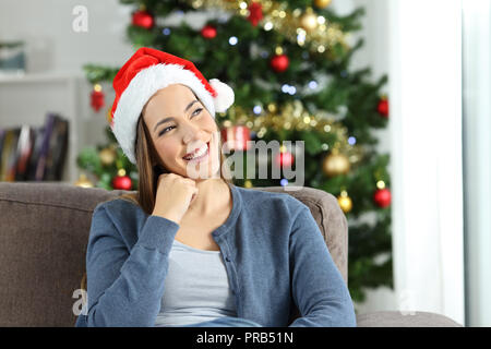 Happy woman thinking on christmas sitting on a couch in the living room at home Stock Photo