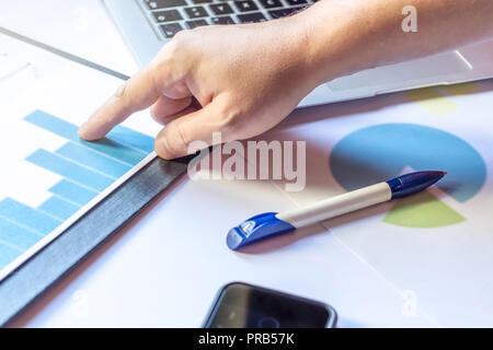 Hand of a young man using a laptop above his charts and notes at the modern office space. Stock Photo