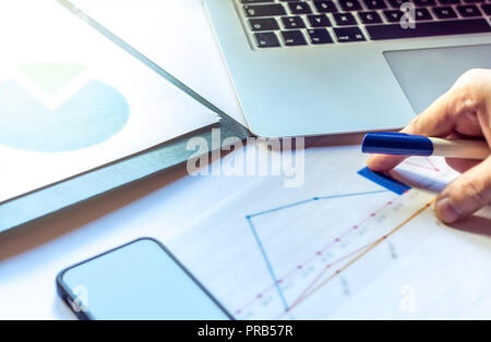 Hand of a young man using a laptop above his charts and notes at the modern office space. Stock Photo
