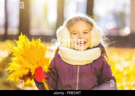 Happy little girl in earflaps with autumn leaves Stock Photo