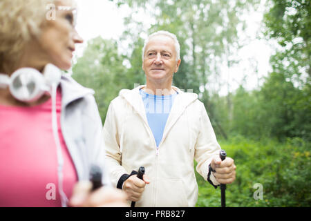 Aged grey-haired man in activewear looking at his wife while trekking in park Stock Photo