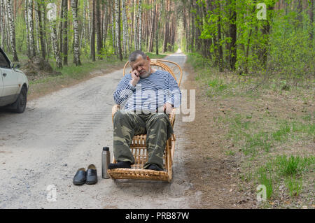 Tired senior driver man resting outside of his car sleeping in a wicker rocking-chair in spring forest Stock Photo