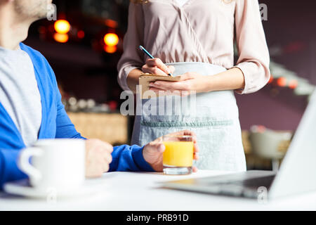 Close-up of unrecognizable waitress in apron making notes while taking order from customer in restaurant Stock Photo