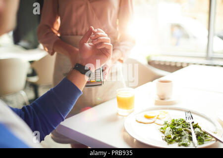 Close-up of unrecognizable man paying for breakfast using smartwatch, he making contactless payment in cafe Stock Photo