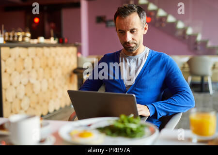 Serious handsome modern male freelancer with stubble using laptop while preparing report in cafe Stock Photo