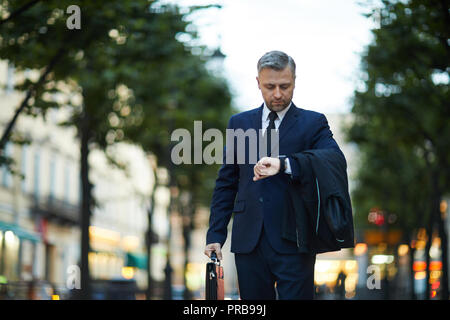 Elegant businessman looking at his watch while moving in the street Stock Photo