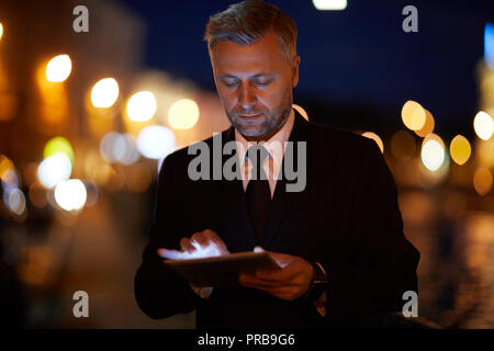 Handsome businessman with tablet searching in the net at night in the city Stock Photo