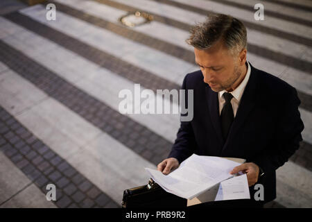 Contemporary financier in formalwear reading papers while crossing road in the evening Stock Photo