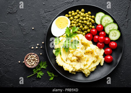 Mashed potato with green peas, tomatoes and boiled egg. Potato puree on plate with vegetables and egg