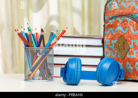 School backpack with school supplies. Books, metal stand for pencils with color pencils and headphones on wooden table. Back to school concept. Stock Photo